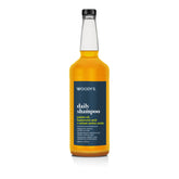 A bottle of Woody's Daily Shampoo featuring a clear glass bottle filled with golden-yellow liquid, a black cap, and a dark navy blue label with white text.