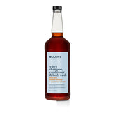 A bottle of Woody's 3-in-1 Shampoo, Conditioner, and Body Wash with a white label and amber liquid, set against a plain white background.