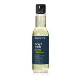 A bottle of Woody's Beard Wash with a dark navy blue label and a black cap, containing a pale yellow liquid, shown on a white background.