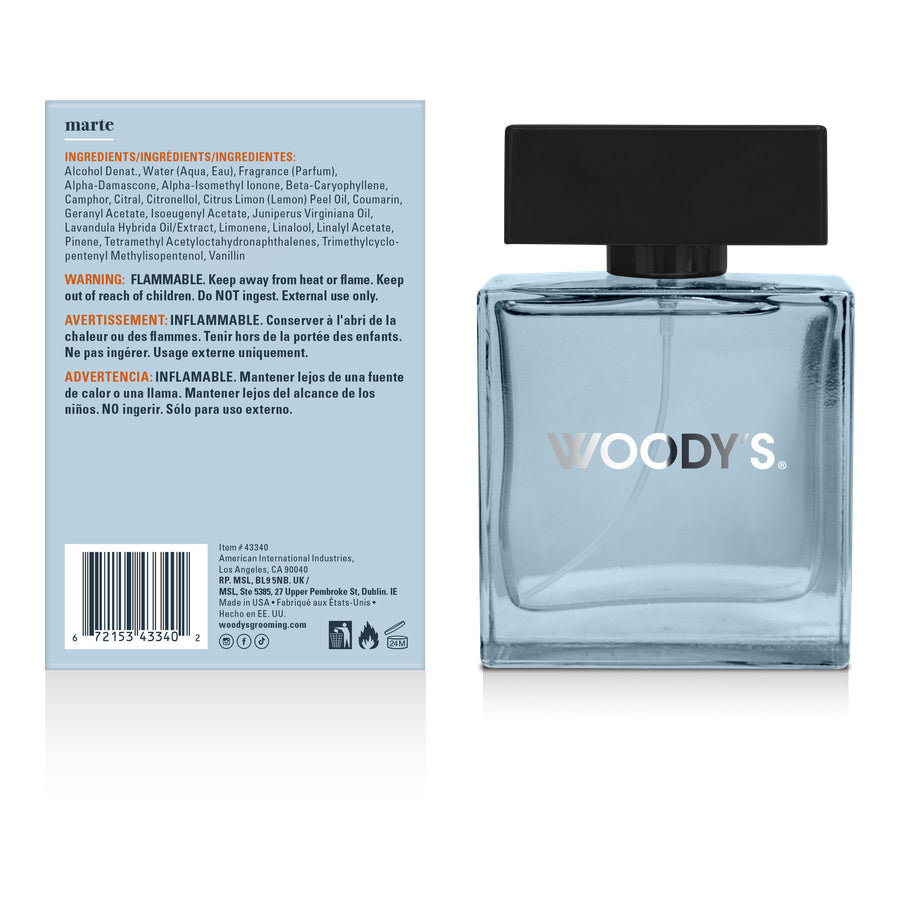 Woody's Eau de Toilette bottle shown next to its back packaging label. The bottle is a light blue translucent glass with a black cap and 'WOODY'S' printed in silver.