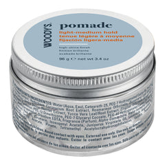 A silver metal jar of Woody's Pomade with a light blue lid label, photographed on a clean white background.
