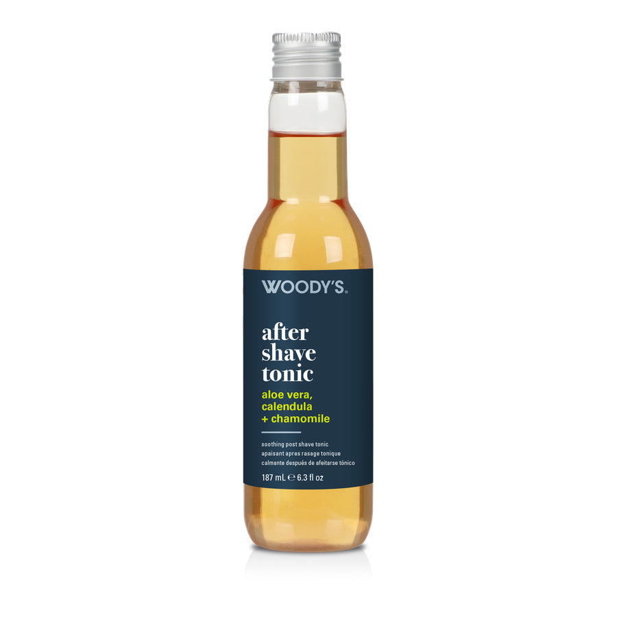 A 127 mL bottle of Woody's After Shave Tonic with a dark navy blue label and a silver cap, containing a golden-amber liquid, shown on a white background.