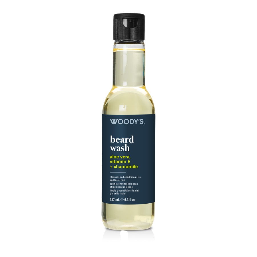 A bottle of Woody's Beard Wash with a dark navy blue label and a black cap, containing a pale yellow liquid, shown on a white background.