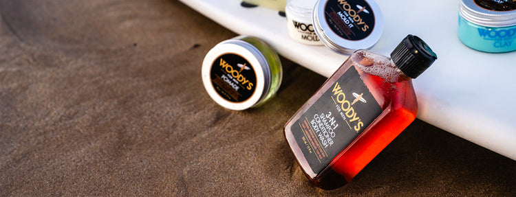Collection of WOODY'S hair care products on a textured surface