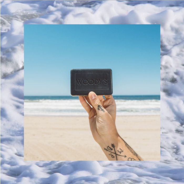 Woody's for Men Activated Charcoal Bar Soap (Beach Scene) displayed against an ocean backdrop for fresh cleansing.
