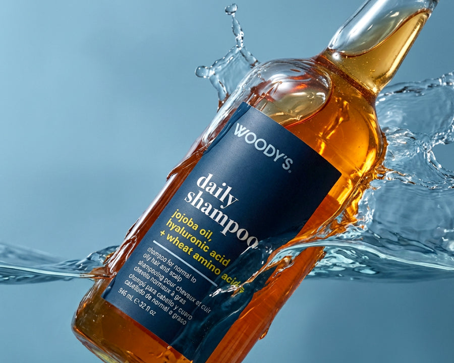 A bottle of Woody's Daily Shampoo floating in splashing water against a light blue background.